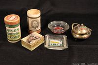 Wide view of all items: two Edison Amberol record tube cases, three ashtrays (two glass, one ceramic), and brass incense burner