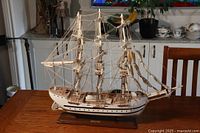 Full side view of the wooden model ship displaying three masts, rigging, and hull detail on a polished wooden table.