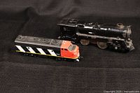 Photo of two locomotives on black fabric background: a black steam locomotive and a red, black, white, and yellow diesel locomotive.