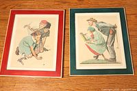 Two framed Norman Rockwell prints side by side, one with red mat and one with green mat, showing children drawing and golf scene, on a white draped surface