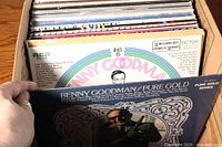 Photo showing a collection of LP records in a box, highlighting Benny Goodman Pure Gold album at the front.