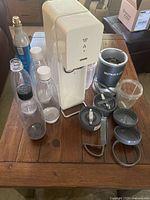 Photo showing SodaStream soda maker, CO2 cylinder, multiple soda bottles, and NutriBullet blender components on wooden table.