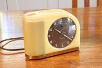 Front and side view of a vintage Westclox electric alarm clock with yellow bakelite casing and brown dial with white numerals and hands, showing the power cord.