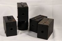 Four vintage box cameras arranged in two groups on a white backdrop, showing front and side views with visible lens apertures and metal clasps.
