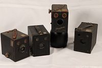 Four vintage box cameras arranged side by side, showing front and top details including lenses, leather handles, and overall condition.