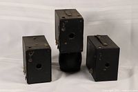 Three vintage box cameras arranged on a plain white background, showing front and side profiles.