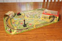Overview of complete tin lithographed train set on table showing train tracks and painted countryside base.