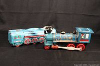 Both vintage tin litho locomotives shown side by side on dark fabric background, highlighting size and overall condition.