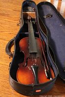 Overall view of the violin in the open case with bow placed inside, front facing upward.