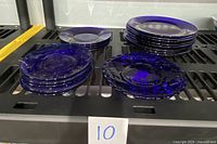 Photo shows multiple stacks of cobalt blue glass plates and saucers on a rack, highlighting the assortment of 18 pieces separated into groups by size and pattern.