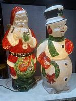 Front view of light-up Santa Claus and Snowman yard decorations on a table, showing details and colors.