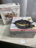 Aroma electric wok box and Mr. Induction induction cooktop box together on table, front view showing product images and details.