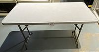 Front view of the 48x24 white plastic folding table with some visible wear.