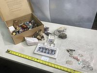 Wide shot showing the opened shipping box with assorted stones, geodes, boxed stones set, and hand-carved animals laid out on a white surface with measuring tape.