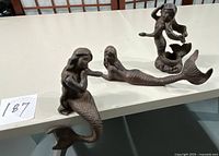 Three cast iron mermaids displayed on a table, showing all items in the lot.