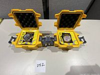 Two yellow hard protective Invicta branded cases with two men's watches inside them, placed on a white surface with lot number 252 in view.