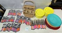 Photo showing the full spread of silverware with colorful handles, two wicker baskets, yellow and red plates stacked