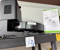 Robot vacuum on charging station with filter pack and manual nearby, showing model and device.