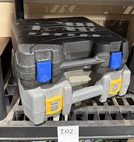 Two closed tool cases stacked, black and gray cases with blue and yellow latches, identified as Ryobi and Dremel tool cases.
