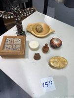 Photo showing all seven items in the lot including Navajo totem, sand art box, small wooden dish with ball, butter stamp, Pueblo pottery, clam-shaped trinket box, and small carved wooden bear figure on a white tabletop.