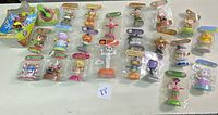 Wide view showing all 22 assorted solar dancing toys and the Scooby Doo bobbing candy dispenser. Figures are individually packaged or boxed and arranged in rows on a white surface.