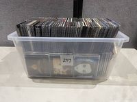 Full plastic storage bin filled with used music CDs arranged upright showing spine titles.