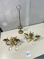 Photo of two brass Victorian style electric wall sconces with crystal drops and one vintage brass oil lamp with tall handle.