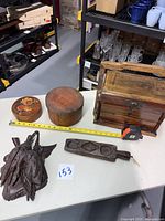 Photo showing all items together on table: two round spice boxes, Chinese wooden carrying box missing front doors, walnut Black Forest duck carving, wooden cookie mold, tape measure for scale.