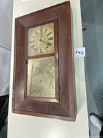 Front view of vintage wooden mantle clock with rectangular wooden frame, clock face with Roman numerals and decorative lower glass panel.