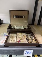 Open jewelry box with multiple compartments containing assorted necklaces, pendants, tie pins and earrings