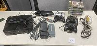 Original Xbox console with disc tray open along with several Xbox controllers, game discs, power cables, and Kinect camera shown on a table.