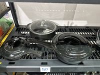 Three black ceramic cookware items on display: two skillets with glass lids and one Dutch oven with lid, all appearing slightly dusty or needing cleaning.