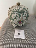 Front view of antique Nippon Japanese porcelain pot showing green base with white raised floral scroll designs and colorful floral panels, including decorative lid and knob.