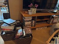 Photo of multiple DVDs stacked in baskets next to a TV stand, showing their arrangement and quantity.