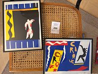 Two framed Henri Matisse prints titled 'Circus' and 'Jazz' shown on rattan chair seats