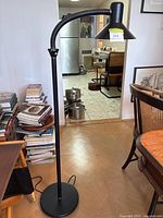 Full view of the black floor reading lamp with bendable gooseneck and round base placed on wooden floor in living room.