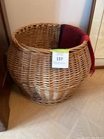 Large round wicker basket with red and beige cloth liners inside, photographed from an angle showing basket shape and weave.