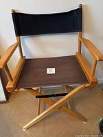 Front view of the vintage directors chair showing wooden armrests, black fabric backrest, and brown fabric seat on foldable wood frame.