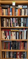 Full bookshelf with assorted books on politics, history, and literature. Wood shelving seen. Books range in size and color.