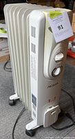 Side/front view of white Noma heater showing fins, control panel, wheels, and power cord.