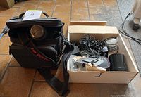 Camera with lens mounted and Pentax carrying case beside it on tile floor