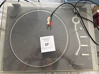 Top view of the record player under the dust cover, showing the platter, tonearm, and RCA cables.