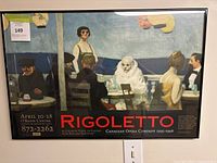 Framed Rigoletto poster showing an outdoor scene with various figures around a table, with opera details and Canadian Opera Company 1995-1996 season text.