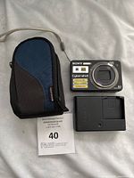 Photo showing Sony Cyber-shot camera, blue and black holder case, and Sony battery charger on light background