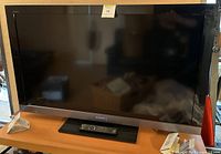 Full front view of the Sony television showing black screen and silver trim at bottom with remote control positioned in front.