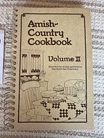 Front cover of the spiral-bound Amish Country Cookbook Volume II showing title and themed illustration.