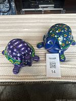 Pair of two colorful hand-painted clay turtle planters placed on a striped surface.