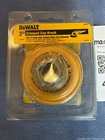Front view of DeWalt 3 inch crimped cup brush in open plastic package with yellow label showing product details.