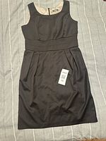 Black sleeveless dress laid flat showing front with visible size tag 58 and pleated skirt detailing.
