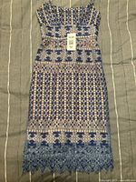 Blue lace dress laid flat showing geometric lace patterns and scalloped edge hem with floral details.